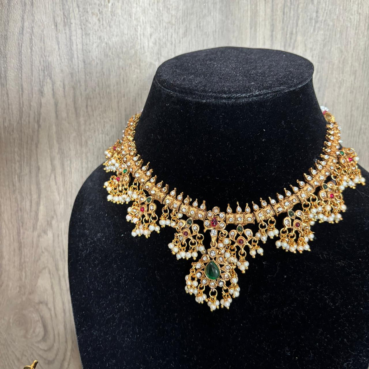 Close up of Women wearing traditional Gold-tone diamond style necklace with green centre stone, ruby accents and pearls cluster