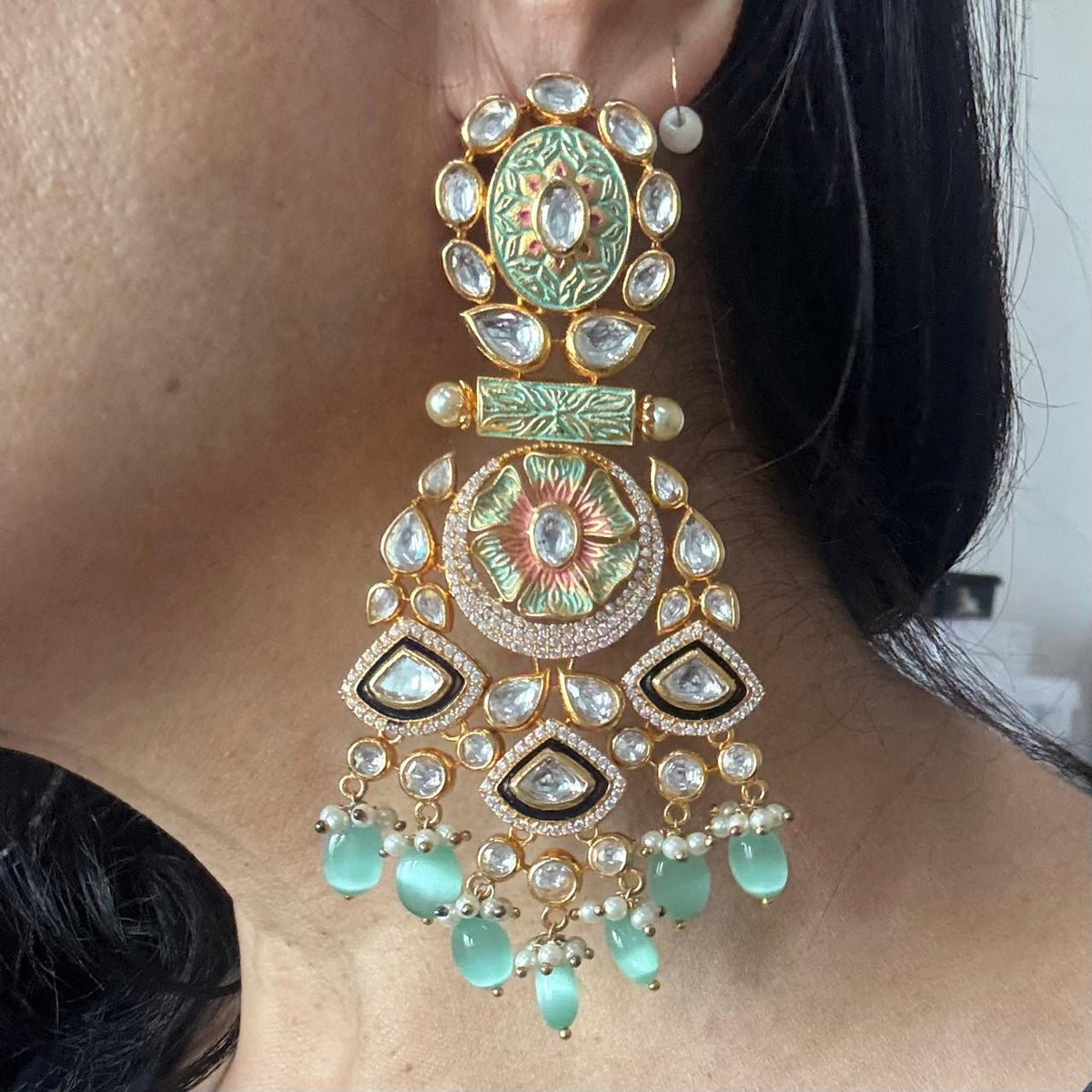 Close up of women wearing Mint green Meenakari-style statement earrings with clear stones and mint green beads drops displayed on a white tray