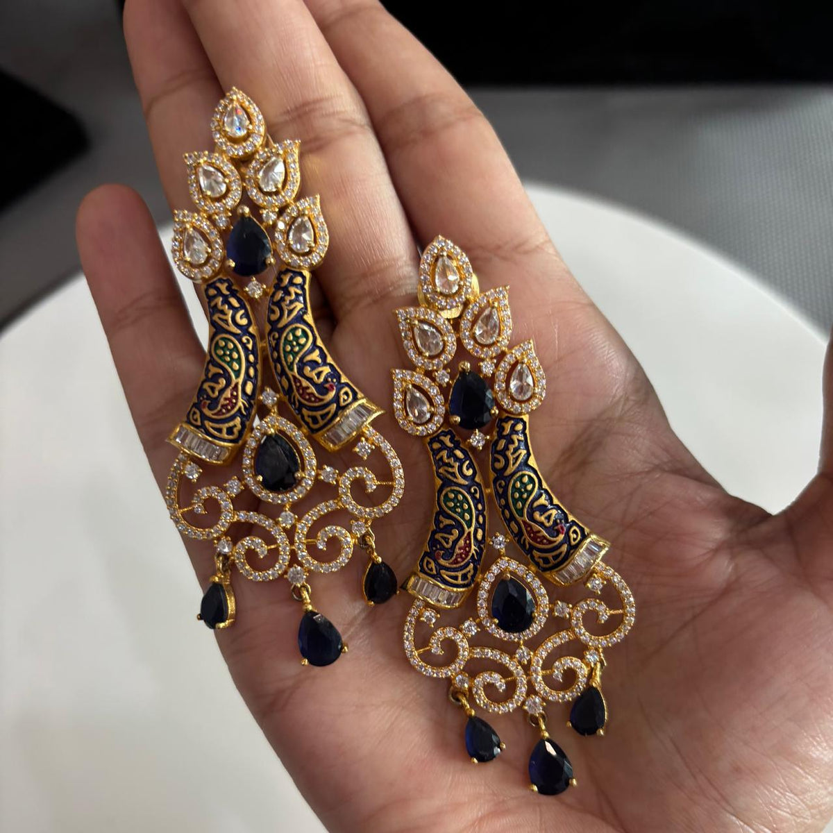 Pair of AD chandelier cocktail earrings on hand with blue stones
