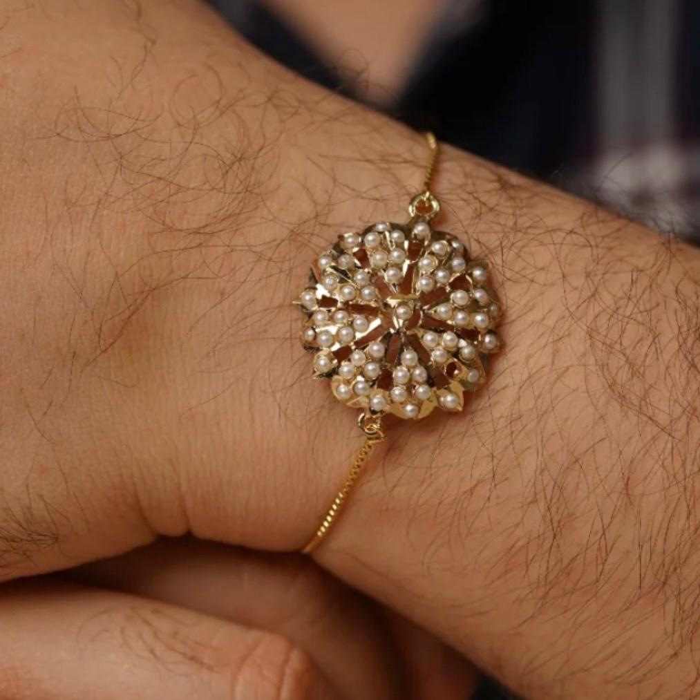 Man wearing Pearl jadau bracelet rakhi in gold tone on wrist