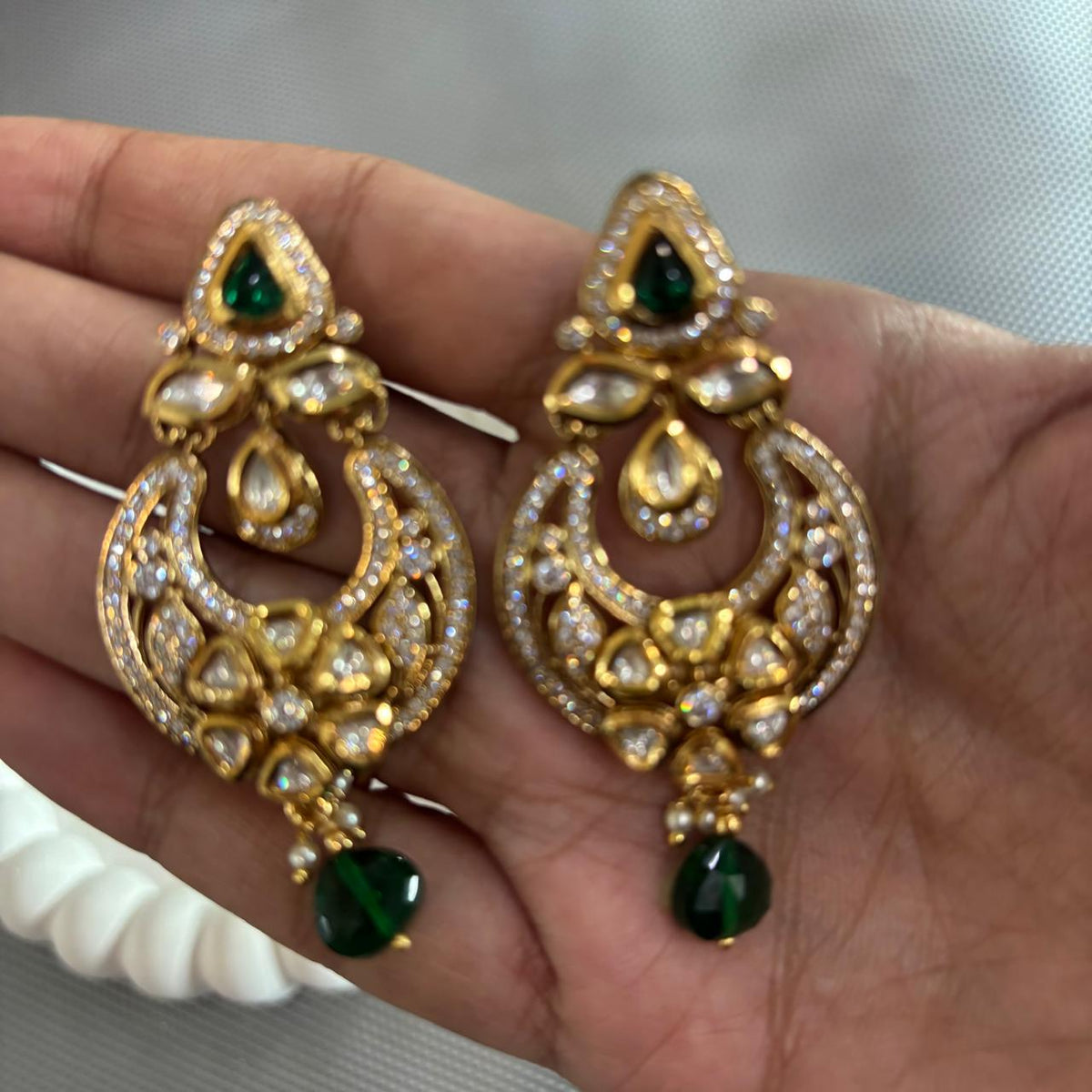 Handheld closeup Polki moissanite chandbali earrings with AD stones and emerald drops