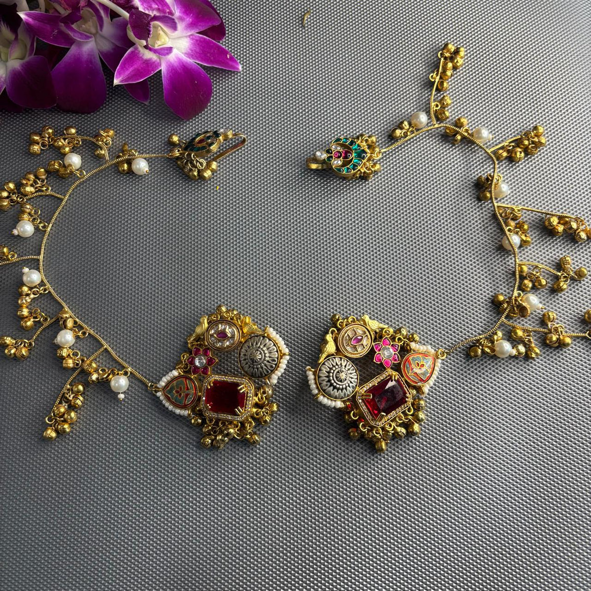 A gold-toned traditional  kashmiri Indian earrings with a matching earchain sahara  hair chain .The earring features a large red stone, a silver-toned circular motif, and small pearl-like beads.