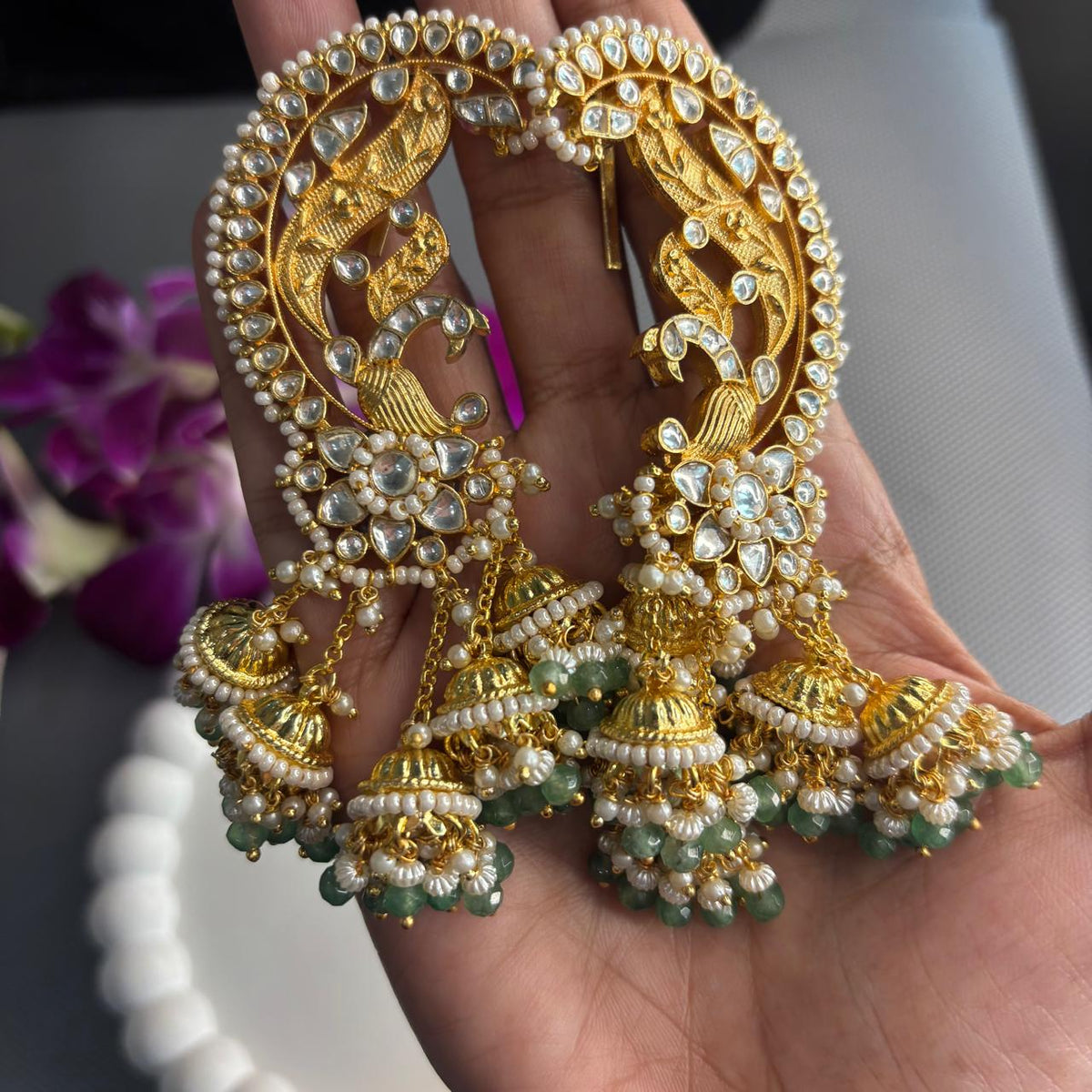 Close up of  Light green Jadau Kundan peacock ear cuff earrings with dangling jhumkas with pearls in hand 