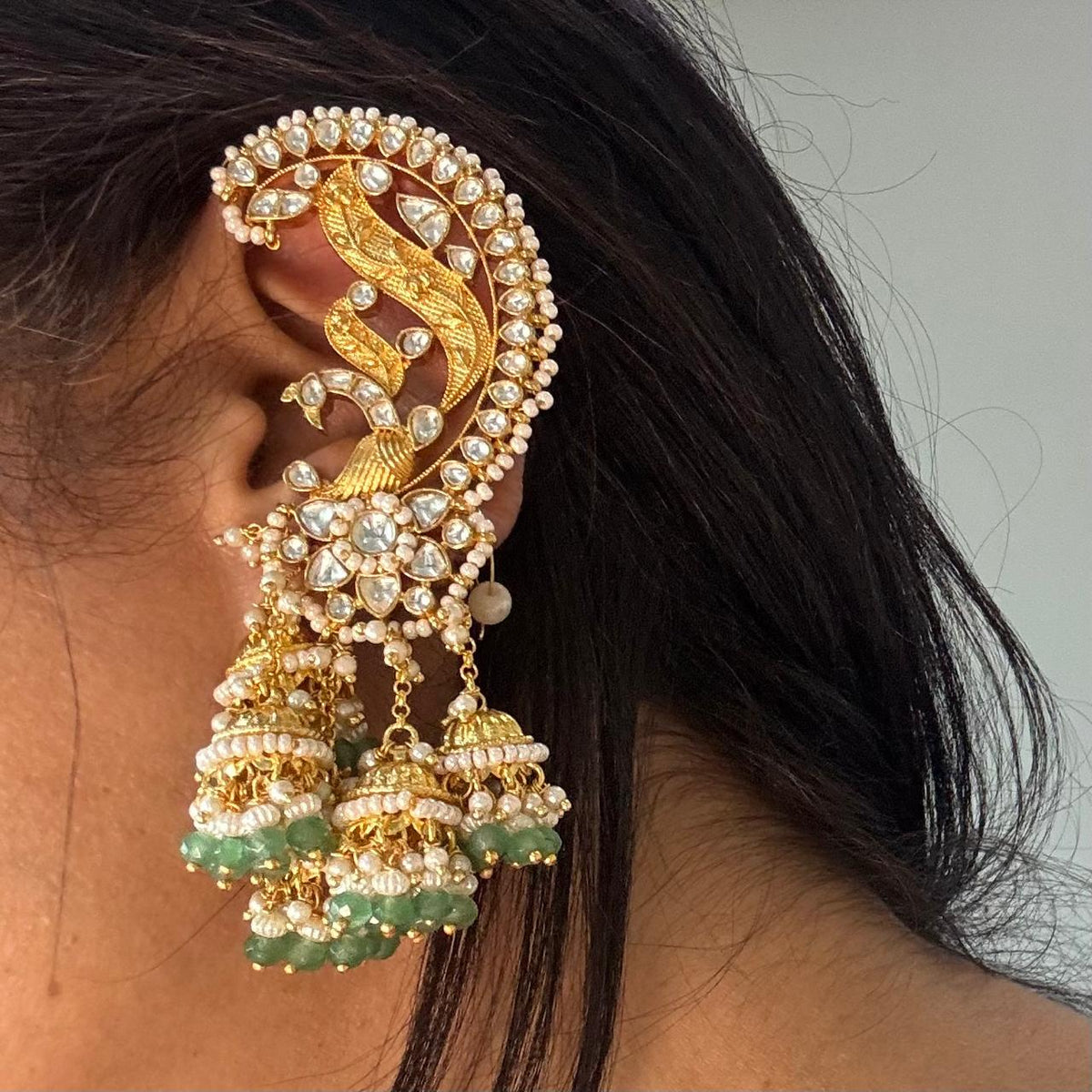 Close up of Woman wearing Woman wearing Light green Jadau Kundan peacock ear cuff earrings with dangling jhumkas
