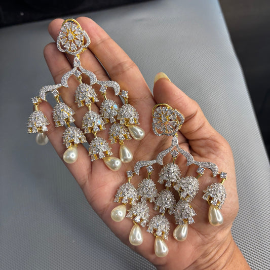 Pair of Meher American diamond chandelier earrings with cascading jhumki tiers and pearl drops held in a hand
