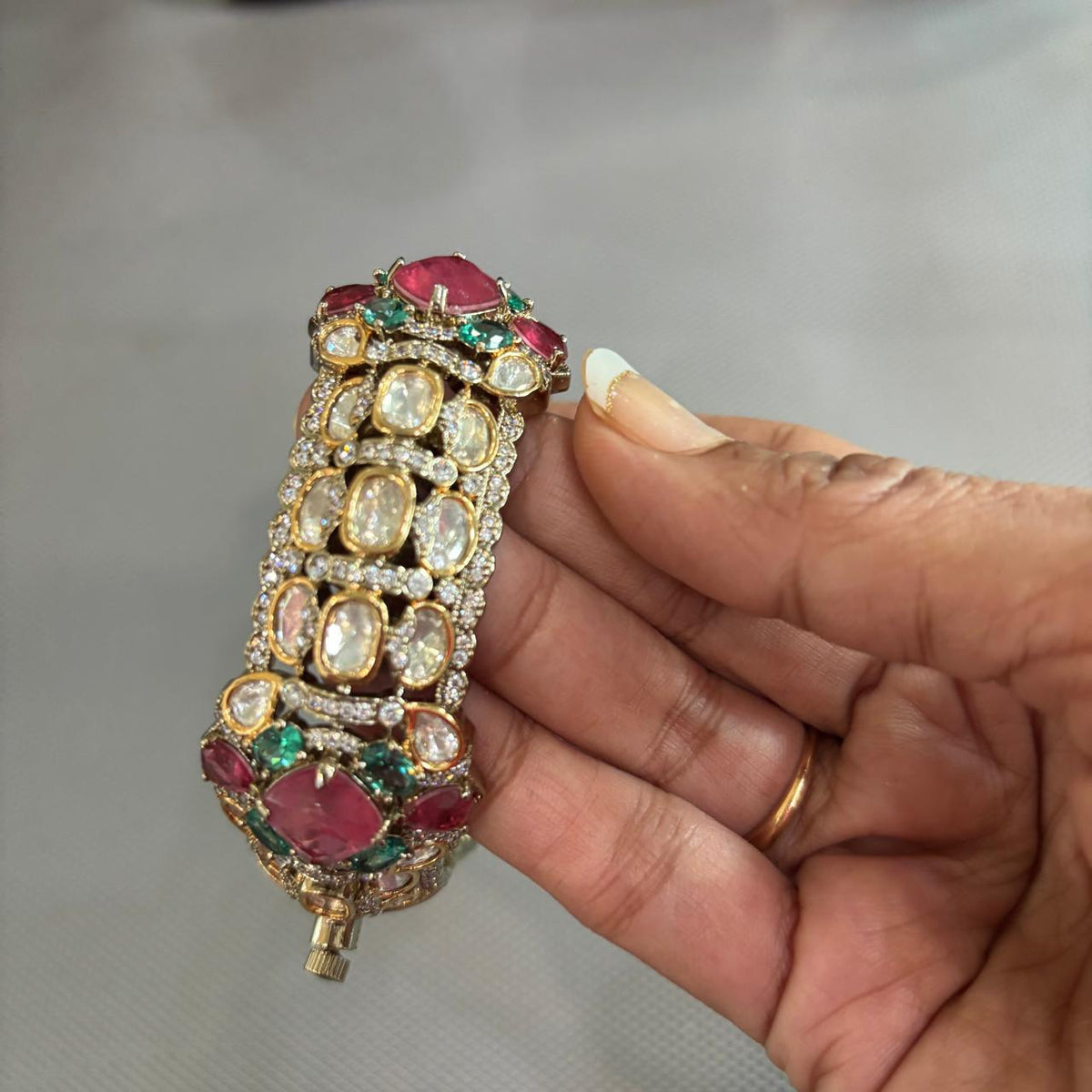 Zevar Polki moissanite-style openable kada held in hand, showing clear stones with pink and green detailing
